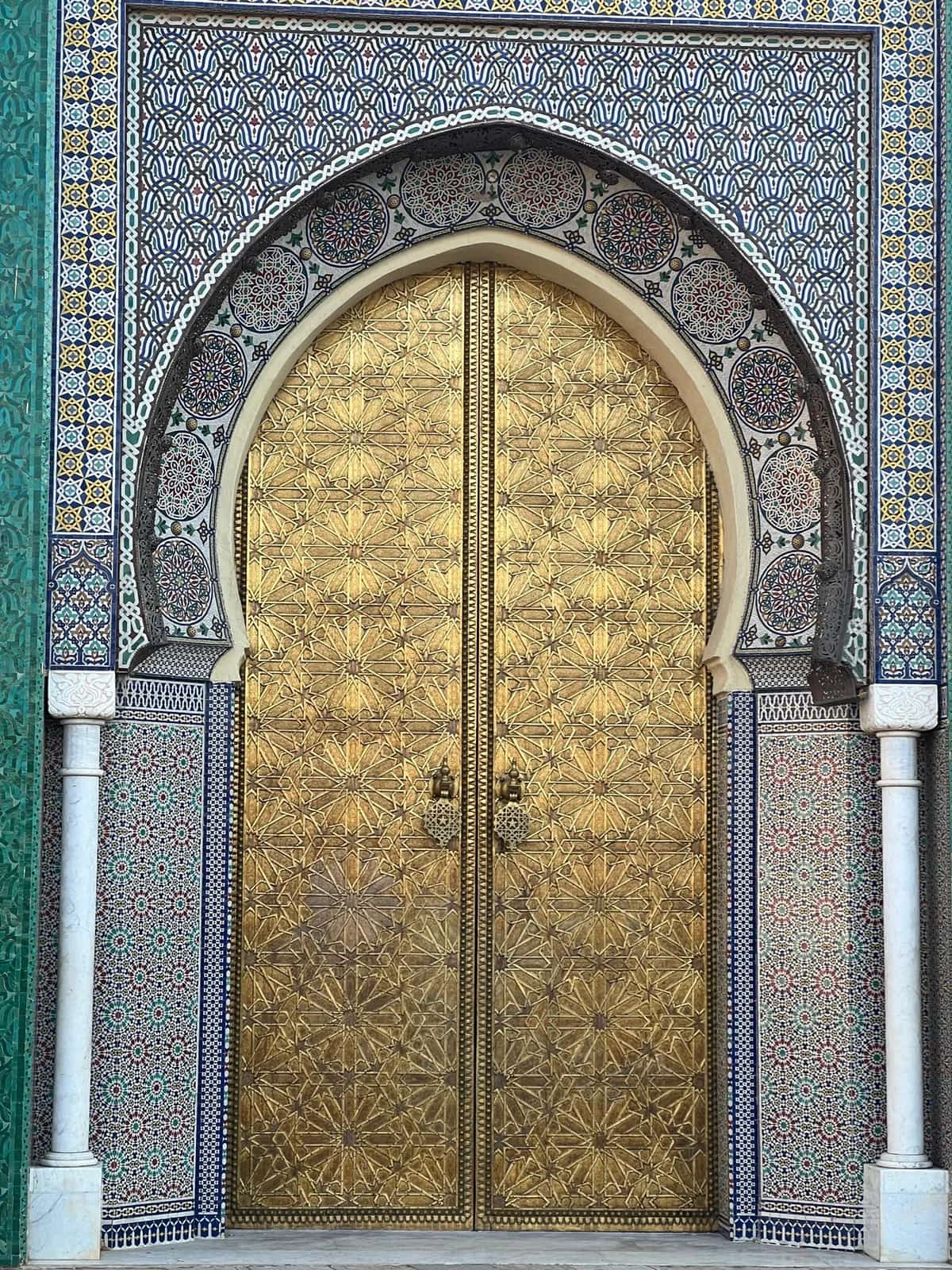 A gold-coloured palace door framed by patterned tilework in Fes