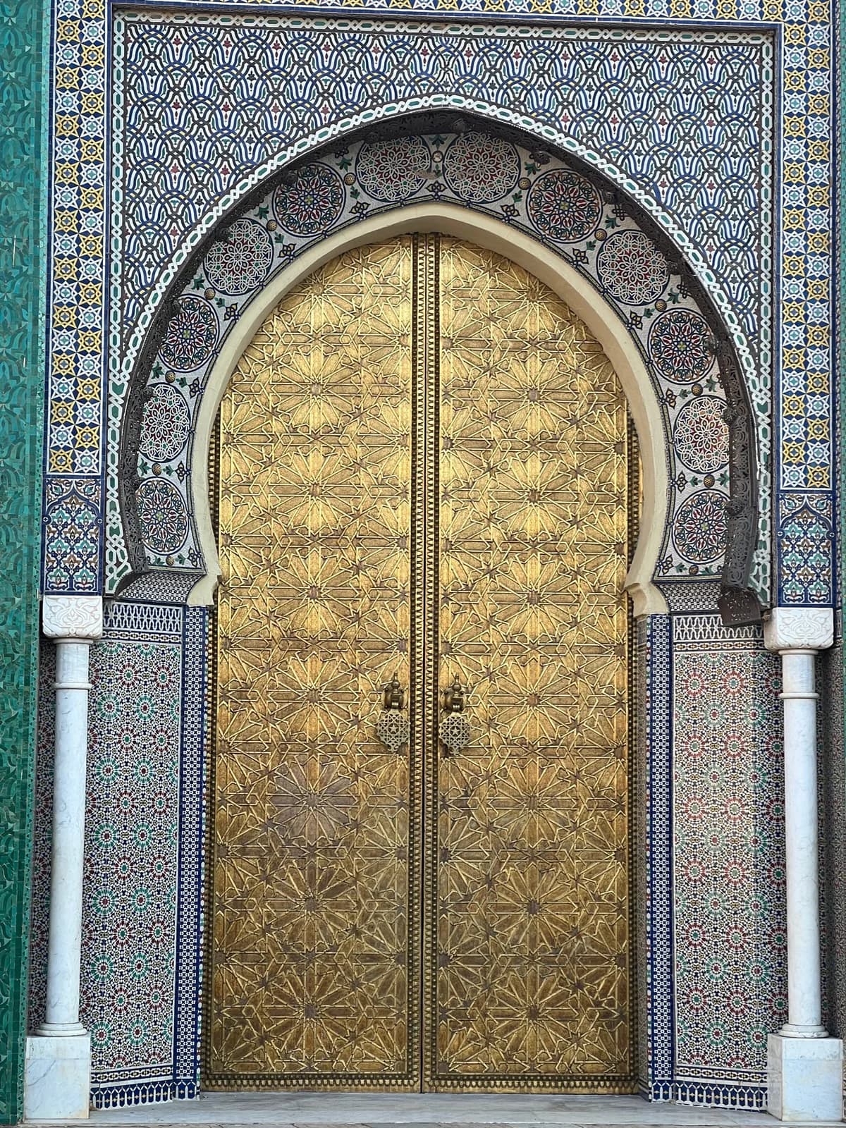 A gold-coloured palace door framed by patterned tilework in Fes