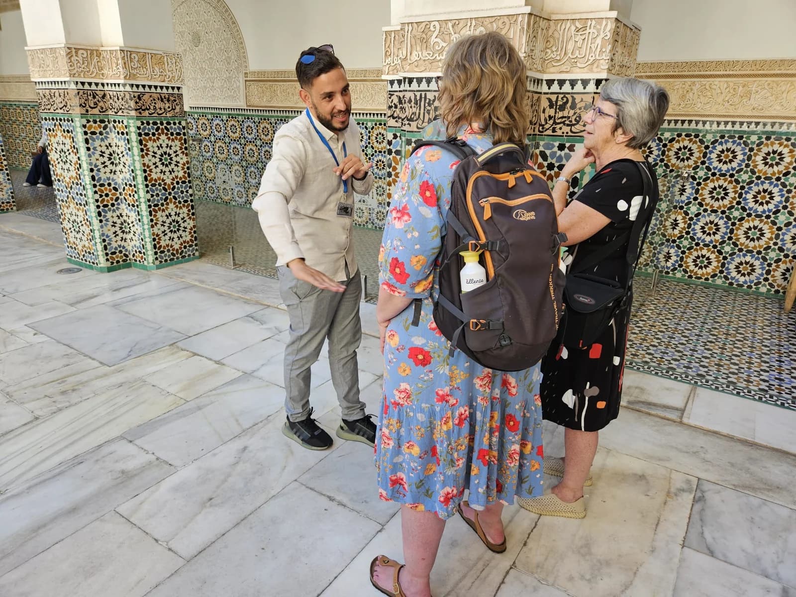 A guide speaking with visitors beside carved walls and tilework in Marrakech